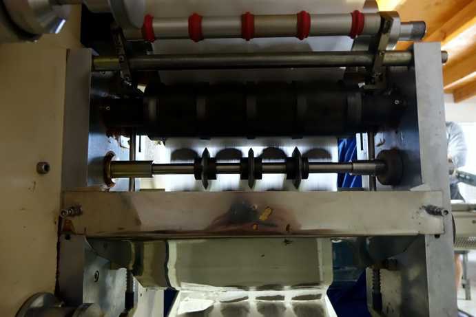 The image shows the tea bag manufacturing machine on Klipfontein Farm from the rear view. Clearly visible are two filter material strips being fed into the machine from above. Between the two layers, the Rooibos tea bag filling can be seen before the machine seals the edges and shapes the individual tea bags.