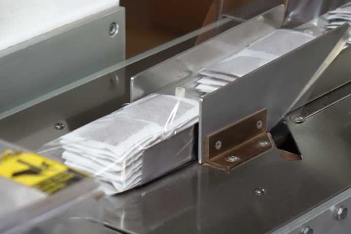 After the machine cuts and perforates strips of four tea bags, workers separate them in the middle, leaving two connected tea bags. These are then stacked in pairs until a stack of ten layers is formed. These stacks are transported via a conveyor belt to the next processing step, where they are wrapped in protective foil and sealed airtight. This protects the tea bags from moisture and preserves their aroma.