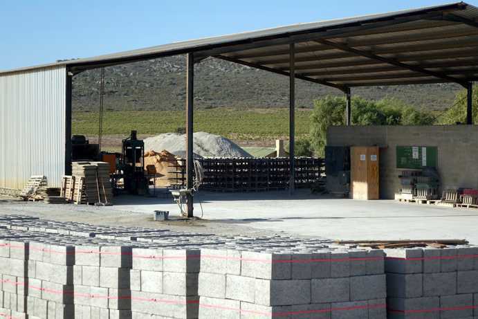 A covered area where concrete hollow blocks are produced. In the foreground, several pallets of ready-to-ship concrete hollow blocks are visible. The production was introduced to provide year-round employment opportunities for seasonal workers.